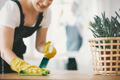 Close-up on smiling housewife with yellow gloves cleaning table with cloth