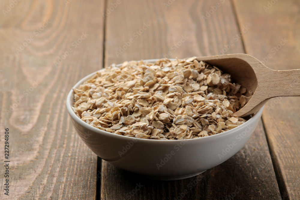 Dry oatmeal in a white bowl and a wooden spoon. food. healthy food. on a brown wooden table. Dry oatmeal in a white bowl and a wooden spoon. food. healthy food. on a brown wooden table.