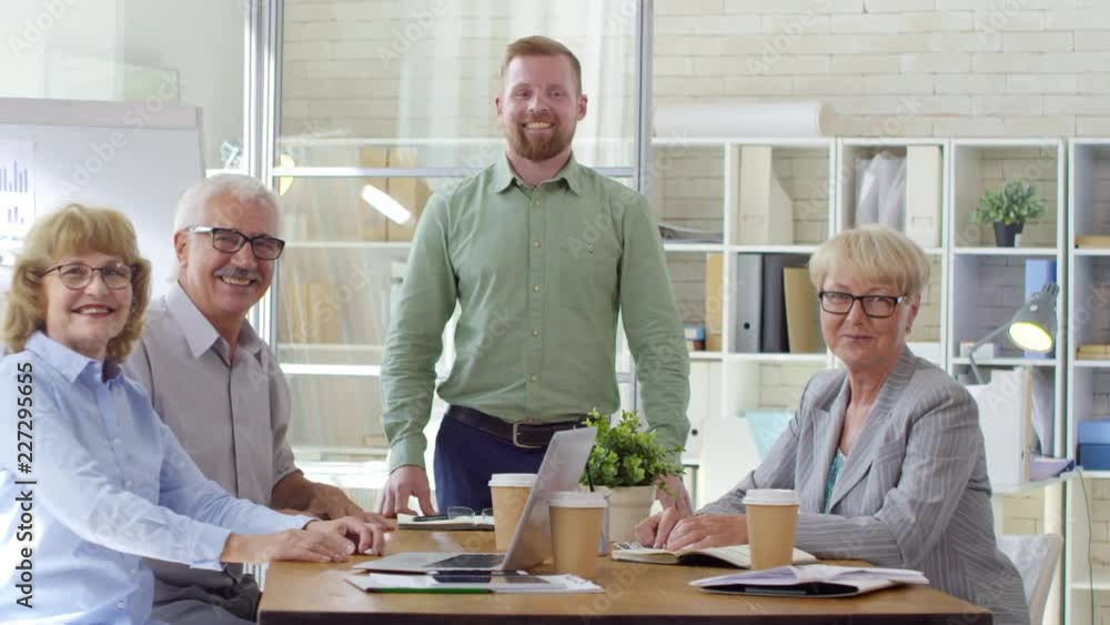 Young CEO and business team of senior professionals looking at camera and smiling while posing at meeting table in the office Young CEO and business team of senior professionals looking at camera and smiling while posing at meeting table in the office