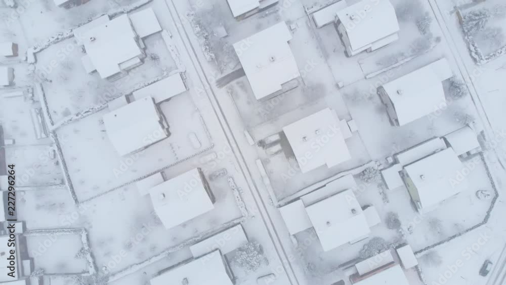 AERIAL, TOP DOWN: Blizzard covers roofs and asphalt roads leading through the tranquil suburbs. Flying above the trails in the snow covered streets and private properties in the idyllic village. AERIAL, TOP DOWN: Blizzard covers roofs and asphalt roads leading through the tranquil suburbs. Flying above the trails in the snow covered streets and private properties in the idyllic village.