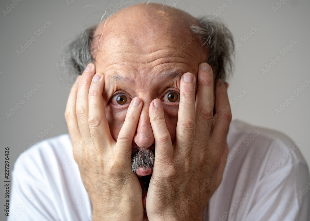Close up of scared and shocked senior man gesturing in fear with hands and face Close up of scared and shocked senior man gesturing in fear with hands and face