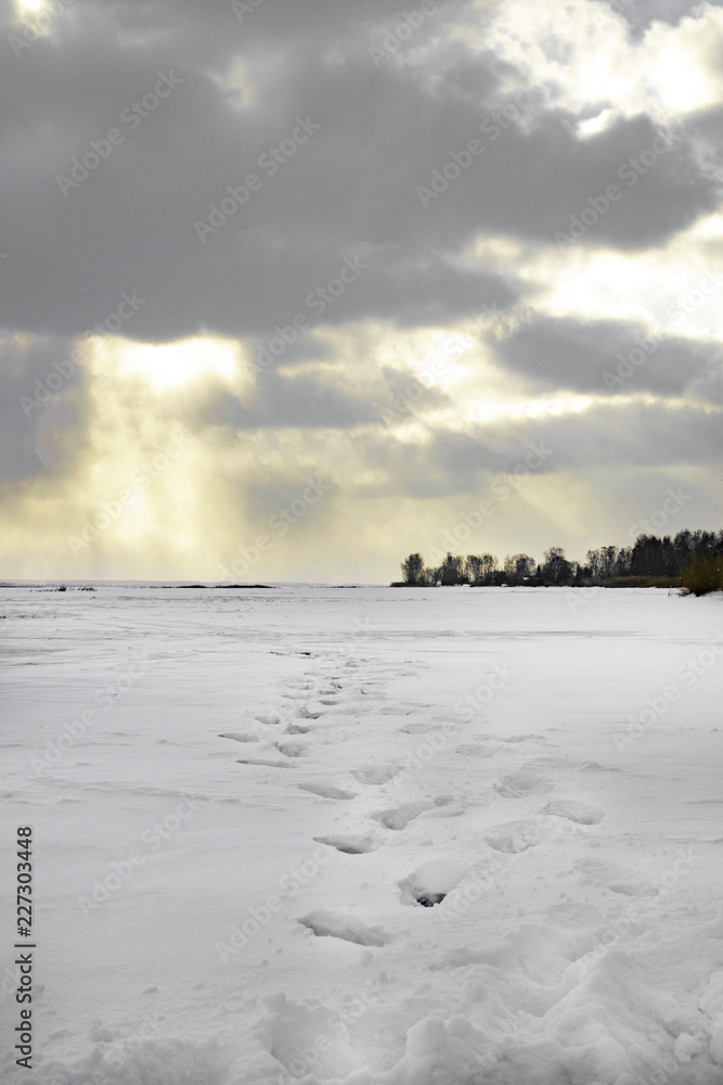 Frosty winter landscape with frozen river or lake. Twilight.Cold morning.Snow covered trees.Sunrise.Footprint. Fresh boots footprints, Background.