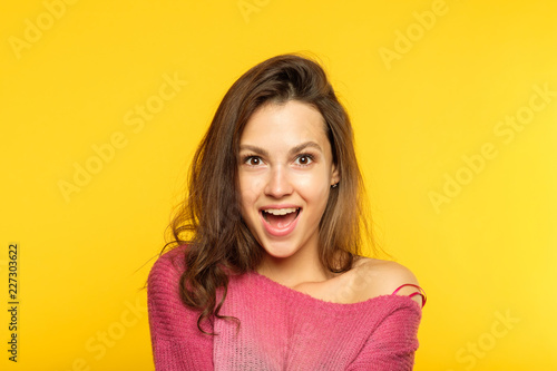 surprised shocked girl. young beautiful woman with brown hair on yellow background. emotional facial expression.