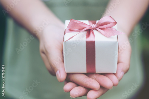 Fototapeta Naklejka Na Ścianę i Meble -  Female hands holding a small gift wrapped with pink ribbon. Selective focus,Selective focus,Valentines day