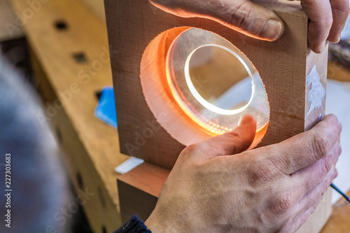 Wood and light, Eco-friendly woodworker's shop. Details and focus on the texture of the material, sawdust, and hands or lighting, while making a futuristic lamp. Mastering wood with peacefullness.