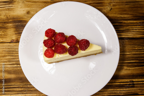 Piece of tasty New York cheesecake with raspberries in a white plate on wooden table. Top view