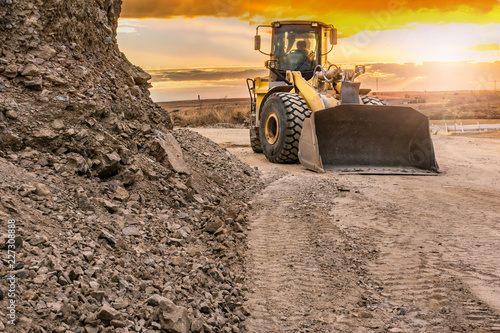 Excavator working on the construction of a road, with the danger of rockfall
