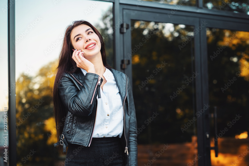 Business woman with smartphone close up near office building. Girl have conversation with cell phone. Beautiful caucasian young woman talking with mobile device.