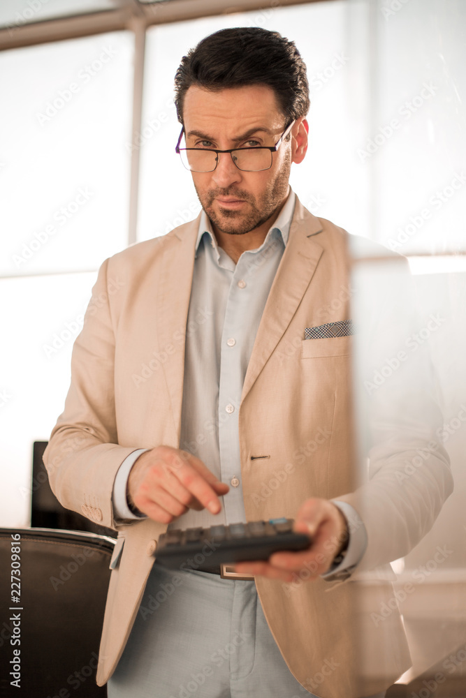 serious businessman using a calculator while standing in the empty office
