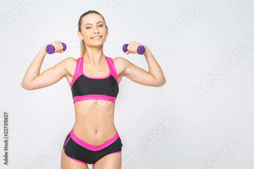 Portrait of happy young fitness woman with dumbbells and perfect body smiling and energetic. Isolated over white background.