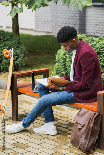 young african american student writing in notebook on street