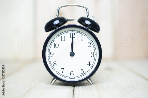 Deadline strait concept with alarm clock set at 12.00 on wooden background.