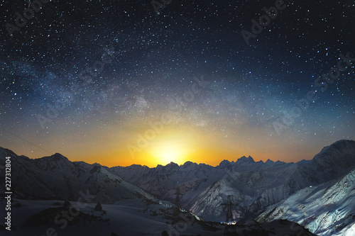 Moonset in the mountains at night with a horizontal milky way on the sky. Snow covered peaks of mountains at night
