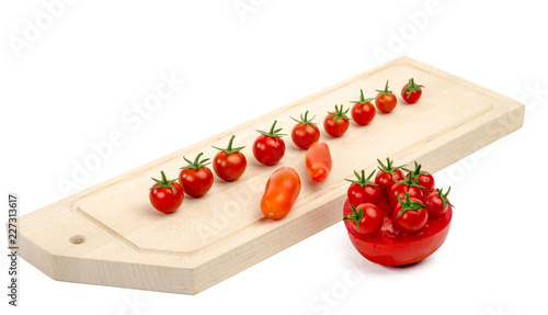 Small tomatoes on a chopping Board, next to half a large tomato with small tomatoes at the top