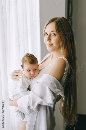 happy mother carrying little baby boy in front of curtains at home © LIGHTFIELD STUDIOS