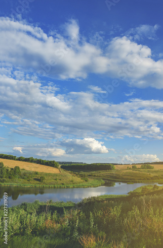 Sunny summer landscape with river,fields,green hills and beautiful clouds in blue sky.