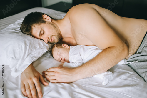 adorable little baby boy sleeping with shirtless father in bed at home