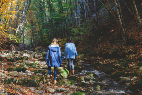 Two young girls friends walking in the autumn forest near the river. Walk in the woods. Girlfriends hiking in the fall. © NesolenayaAleksandra