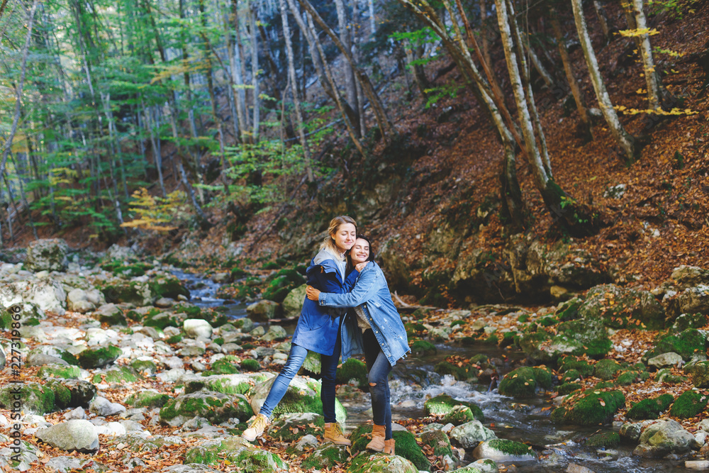 Two young girls friends walking and having fun in the autumn forest. Walk in the woods. Girlfriends hiking in the fall, laugh and hug. Two young girls friends walking and having fun in the autumn forest. Walk in the woods. Girlfriends hiking in the fall, laugh and hug.