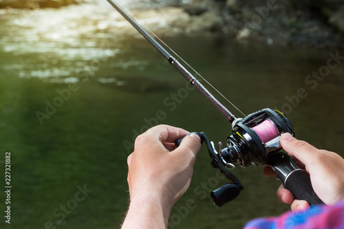 Fishing reel multiplier with a fishing rod in the hands of the fisherman. Trout fishing in the river. Close up.