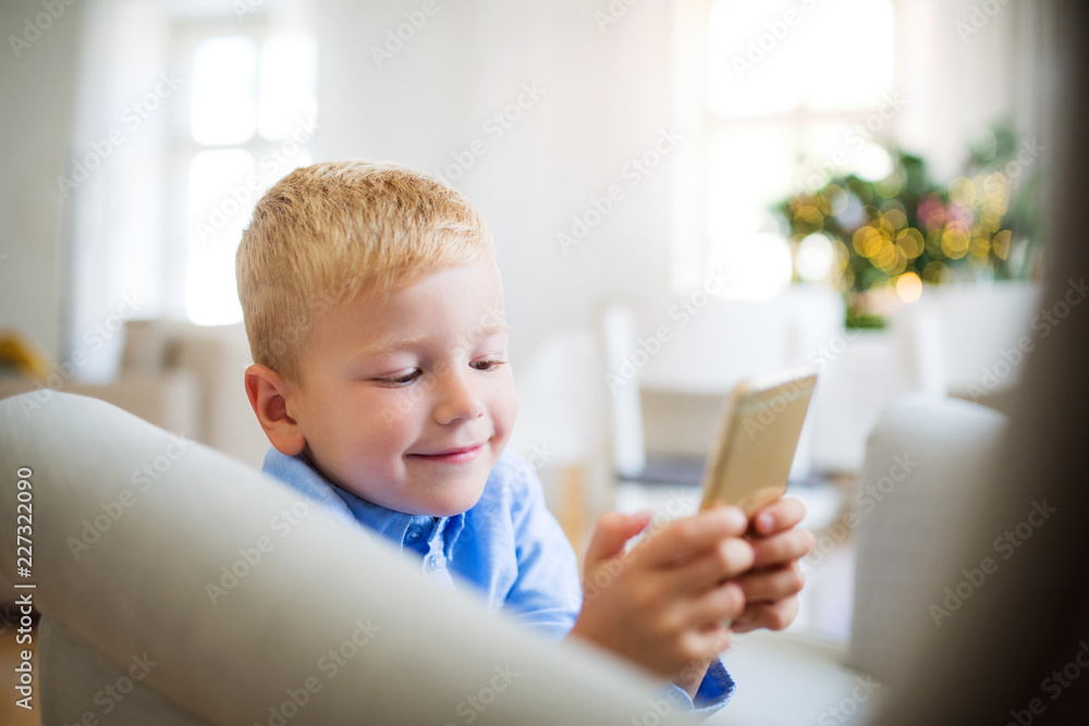 A small boy with smartphone sitting on an armchair at home at Christmas time. A small boy with smartphone sitting on an armchair at home at Christmas time.