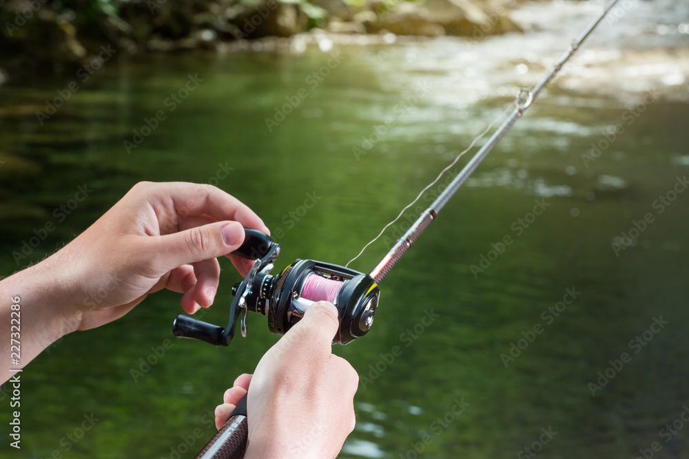 Fishing reel multiplier with a fishing rod in the hands of the fisherman.  Trout fishing in the river. Close up. Stock Photo