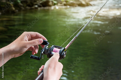 Fishing reel multiplier with a fishing rod in the hands of the fisherman. Trout fishing in the river. Close up.