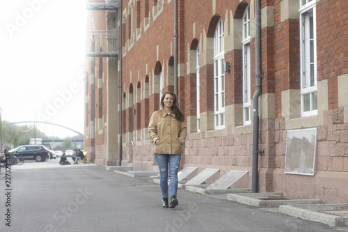 Junge Frau gehend an einem alten Gebäude aus Backstein © SundGo