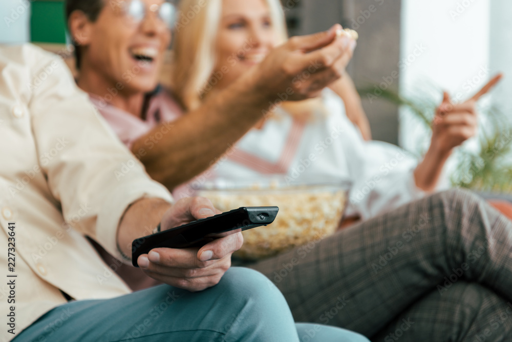 cropped shot of mature friends using remote controller and eating popcorn while watching tv together cropped shot of mature friends using remote controller and eating popcorn while watching tv together