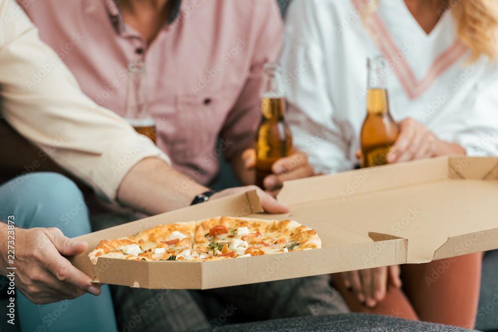 cropped shot of man holding pizza box and friends drinking beer behind