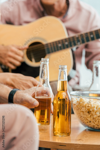 cropped shot of mature friends drinking beer and playing acoustic guitar