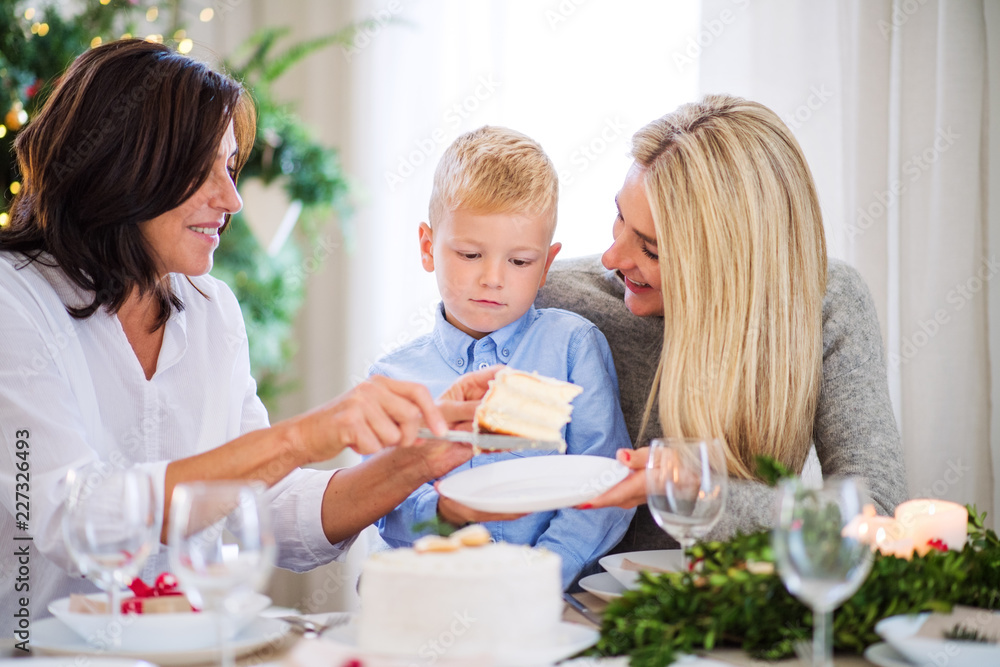 A small boy with mother and grandmother eating a cake at Christmas time.