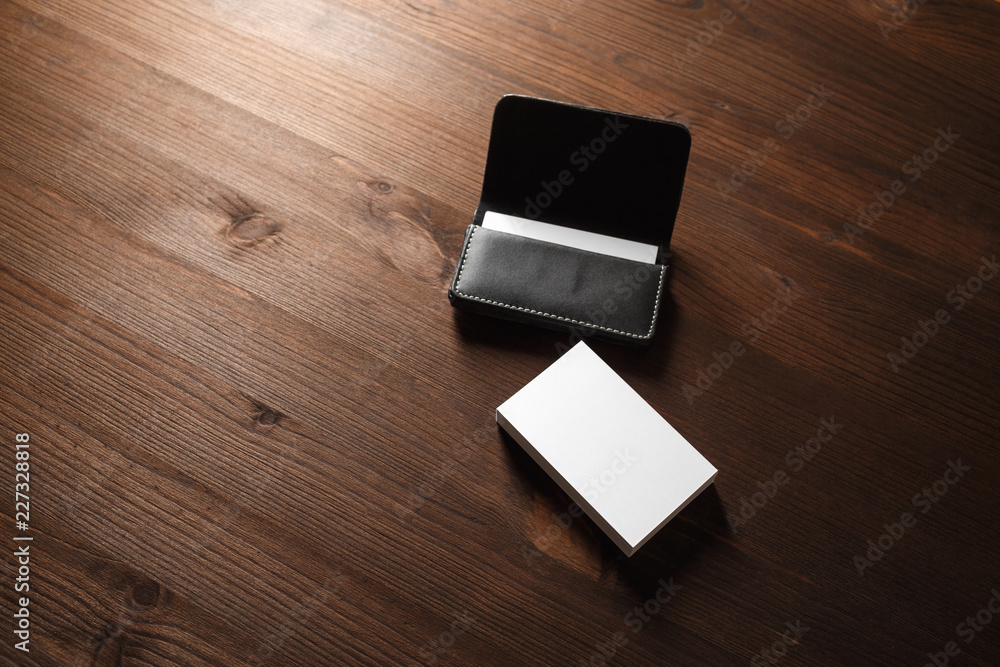 Black leather card holder with blank white business cards on wood table background. Black leather card holder with blank white business cards on wood table background.