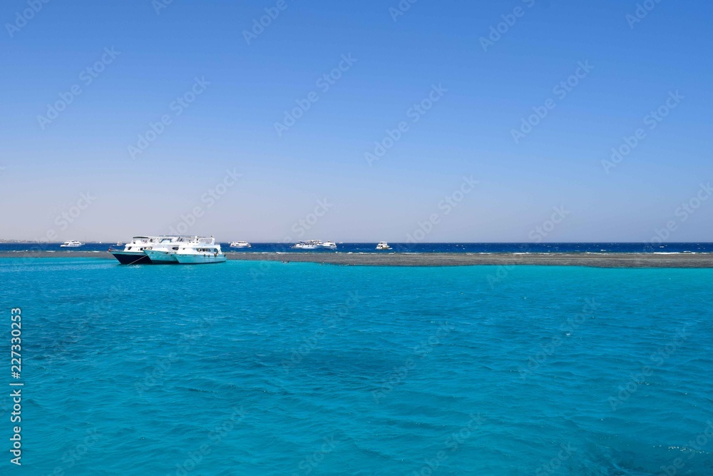 Boats in the Red Sea in front of a reef in turquoise ocean, snorkeling destination for tourists in Egypt