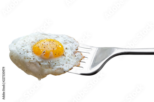 Single fried egg sprinkled with ground black pepper resting on metal spatula isolated on white.