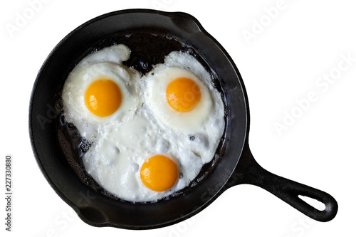 Three fried eggs in cast iron frying pan isolated on white from above.
