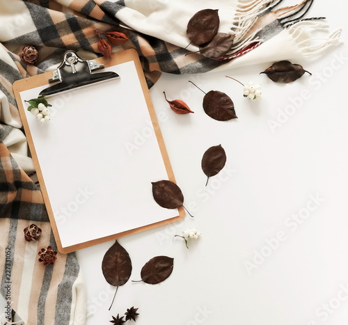Autumn background with mock up clipboard, scarf in a cage and autumn leaves on a white background. Flat lay. Top view. Copy space