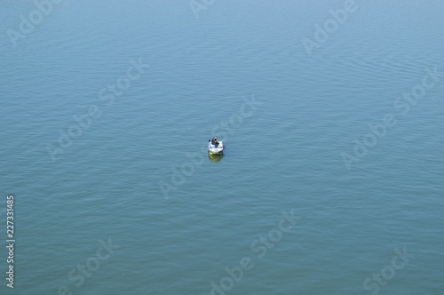 Fisherman in boat, alone on quiet, blue water