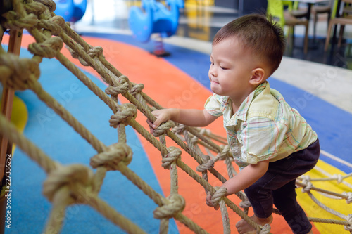 Cute little Asian 2 years old toddler baby boy child having fun trying to climb on jungle gym at indoor playground, Physical, Hand and Eye Coordination, Sensory, Motor Skills development concept
