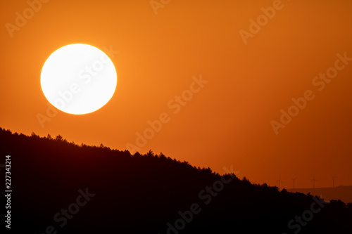 Big sun circle at dusk over mountains with orange sky