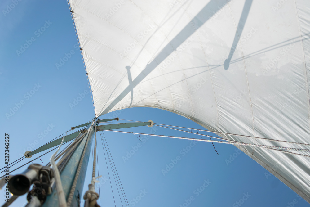 White sail of a sailing boat against sky. Sails of river sailing yacht in the wind against the blue sky White sail of a sailing boat against sky. Sails of river sailing yacht in the wind against the blue sky