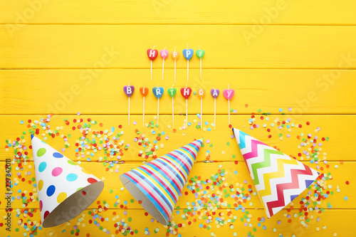 Birthday paper caps with candles and confetti on yellow wooden table