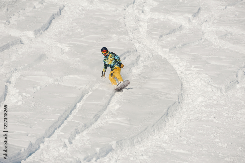Snowboarder in bright sportswear riding down a snow hill on bright winter day
