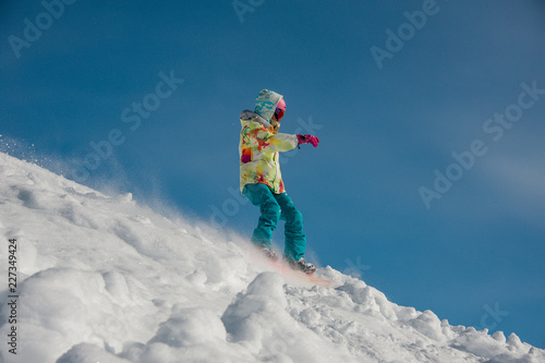 Woman snowboarder in bright sportswear riding down the mountain slope against the blue sky