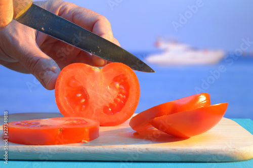 chopping a tomato on cutting board on the beach at sunset