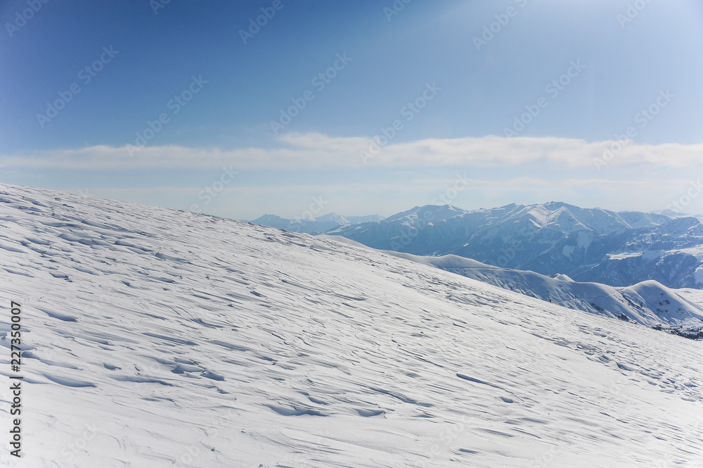 High pure winter mountains and hills covered with snow under the bright blue sky