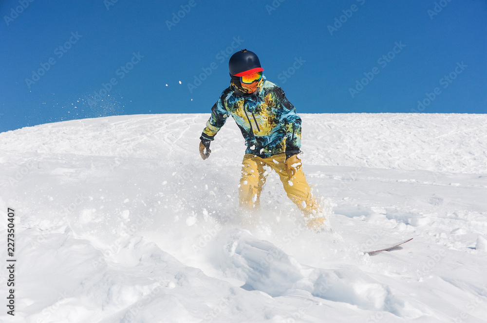 Professional snowboarder in bright sportswear riding down a mountain slope Professional snowboarder in bright sportswear riding down a mountain slope