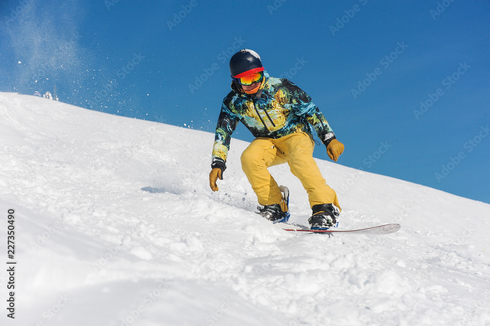 Snowboarder in bright sportswear riding down a mountain slope