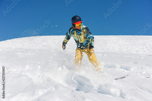 Professional snowboarder in bright sportswear riding down a mountain slope