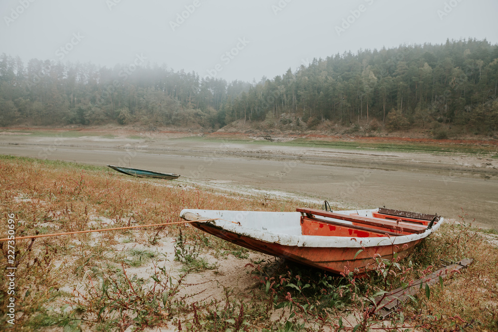 Anchored abandoned old fishing red boat on the bank of the empty Orlík Reservoir in foggy autumn day Anchored abandoned old fishing red boat on the bank of the empty Orlík Reservoir in foggy autumn day